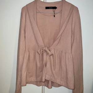 Rosa kofta med knyt från Vero Moda - Supersöt rosa kofta från Vero Moda i storlek S. Koftan har långa ärmar, volang nedtill och ett snyggt knyt framtill som ger en chill och feminin vibe. Perfekt att slänga över en topp när det är lite kyligt ute. Materialet känns mjukt och skönt mot huden.