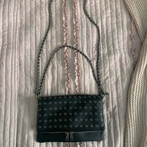 Svart axelväska med nitar och kedja - Cool svart axelväska i skinn med silverfärgade nitar över hela framsidan och två grova kedjor som axelrem som går att knäppa loss. Den har två stora fack och liknat zadig väskan i modellen💗 Kedjan har rostats lite därav priset!