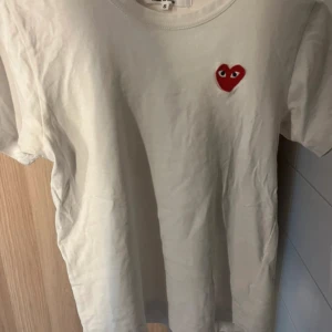 Vit t-shirt Comme des Garçons Play - Vit t-shirt från Comme des Garçons Play med det ikoniska röda hjärtat med ögon broderat på bröstet. Klassisk rund hals och korta ärmar. Perfekt basic med en cool detalj som sticker ut. Strlk S men skulle säga att den är mer som xs. Jätte jätte snygg att ha under en kofta typ eller utan något över!!