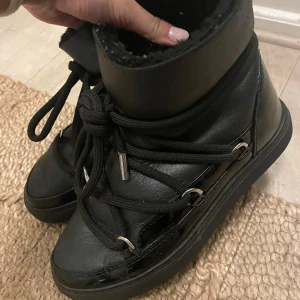Svarta Moon Boots från Inuikii - Säljer ett par svarta Moon Boots från Inuikii med glansig finish och grova snören som går runt hela skon. Insidan är fodrad med mjukt material och yttersulan är platt och robust. Perfekta för kalla dagar och har en cool urban vibe. Ordinarie pris 4500kr