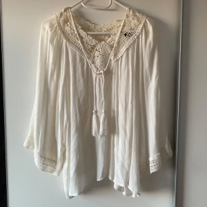 Vit boho blus med spets och knyt - Superfin vit blus i boho-stil med breda trekvartsärmar och vackra virkade spetsdetaljer vid halsringning och ärmslut. Aldrig använd. Passar xs och s
