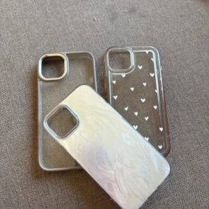 Iphone 13 mobilskal (3st för 50kr) - Säljer mobilskal för Iphone 13.  🤍 Skal 1: Genomskinligt skal med ljusbruna/beige kanter och gulddetaljer kring kamera och knappar. Skalet är från H&M och är i väldigt bra skick.  ~ Enskilt pris 30kr ~ 🤍 Skal 2: Silvrigt glänsande skal med pärlemor mönster. Kanter och knappar är genomskinliga. Skalet är från Shein och är i väldigt bra skick. ~ Enskilt pris 20kr ~ 🤍 Skal 3: Genomskinligt skal med små vita hjärtan. Skalet är från Shein. Lätt missfärgat men inget större.  ~ Enskilt pris 15kr ~