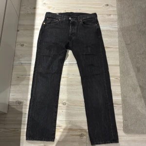 Levi's 501 svarta jeans W31 L30 - Svarta Levi's 501 jeans.  Jeansen har knappgylf och den ikoniska läderpatchen bak i midjan. Materialet är slitstark denim i bomull och färgen är mörkt svart med subtila tvättade detaljer.