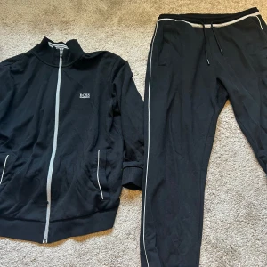 Hugo Boss Dress Svart/Vit - Schysst mjukisdress från Hugo Boss. Sparsamt använd. Koftan är L och byxorna XL. Originalpris: ca 1500kr