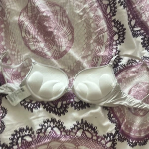 Vit Push-up bh från H&M, 75A - Snygg vit bh från H&M i storlek 75A. Den har vadderade kupor med bygel och smala axelband som går att justera. Materialet är mjukt och stretchigt, tillverkat av 85% polyamid och 15% elastan. Perfekt för sköna underkläder! Pris går att diskutera. Lite missfärgad av en tröja på sista bilden men syns inte om du har på dig den. 