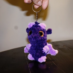 Virkad nyckelring drake  - En virkad lila drake med nyckelring. Perfekt att hänga på väskan eller kanske hänga på nyckeln så de inte tappas bort?