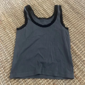 Grå linnetopp med spets från Brandy Melville - Supersnygg grå topp från Brandy Melville med svarta spetsdetaljer runt halsringning och axelband. 