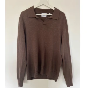 Brun pikétröja från Bläck - Snygg brun pikétröja från Bläck med klassisk krage och v-ringad hals. Tröjan har långa ärmar och ribbade muddar vid ärmslut och nederkant. Perfekt för dig som gillar en chill och stilren look.