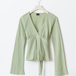 Ljusgrön omlottopp - Säljer helt ny med prislapp omlottopp från Ginatricot i sorlek S med v-ringad hals och långa ärmar. Toppen har knytband i midjan ❤️❤️