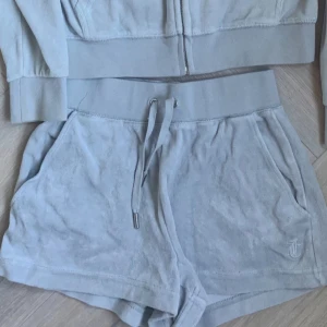 Ljusgrå velourshorts Juicy Couture XS - Snygga ljusgrå shorts från Juicy Couture i mjuk velour med bred resår i midjan och snörning framtill. Klassisk JC-brodyr på benet och två sidofickor. Perfekta för chill eller sportig stil, riktigt comfy och trendiga. RIKTIGA säljer även matchande överdel 