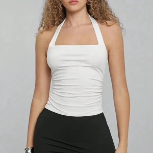 Vit halterneck linnetopp - Säljer vidare då den inte passande. Snygg vit halterneck linnetopp med raka linjer och smickrande rynkade sidor. Toppen är ärmlös och har öppen rygg, perfekt för varma dagar. Tillverkad i mjukt och stretchigt material som sitter tight och bekvämt. 