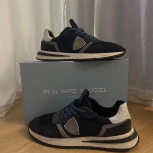 Philippe Model TROPEZ - Snygga sneakers från Philippe Model i marinblått med grå och vita detaljer. Skorna har snörning, rund tå och platt sula. Materialmix av mocka och syntet ger en cool och sportig vibe. Perfekta för dig som gillar stilrena och trendiga sneakers.