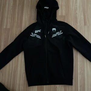 UFC hoodie från Venum - Svart hoodie från Venum med UFC-logga och vita detaljer på bröstet.  Storlek S, skick 9/10. Köpt för 900 på jabb.se (just denna modell är slutsåld) Skriv för fler bilder (pris kan diskuteras) perfekt inför träning eller till vardags! Skulle säga att den passar dig som är 165-175 typ