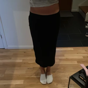 Svart ribbad långkjol med slits - Säljer en svart långkjol med ribbad struktur och en snygg slits baktill. Kjolen har en rak passform och är gjord i ett mjukt stickat material som sitter skönt i midjan. Perfekt för dig som gillar stilrena och enkla plagg med lite edge.