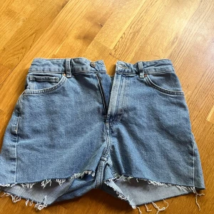 Blåa shorts i storlek S/34 - Säljer ett par klassiska blå jeansshorts från Never Denim i modell mid short. De har fransiga kanter och femficksdesign. Midja i midwaist och nästan aldrig använda. 
