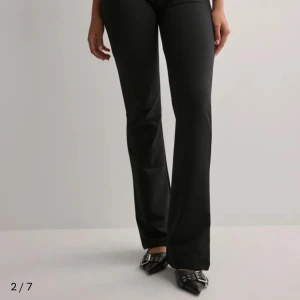 Svarta bootcut byxor med hög midja - Säljer ett par svarta bootcut byxor från Gina Tricot med hög midja och två knappar framtill. Byxorna har en snygg, figurnära passform upptill och vida ben nedtill. Materialet är mjukt och stretchigt, perfekt för en trendig och bekväm look.