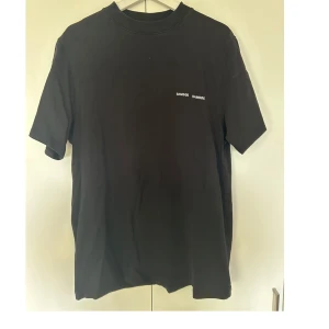 Svart t-shirt från Samsøe Samsøe - Svart t-shirt från Samsøe Samsøe med diskret logga tryckt på bröstet. Klassisk rund hals och korta ärmar. Tillverkad i mjuk bomull som är skön mot huden. Perfekt för en clean och enkel stil.