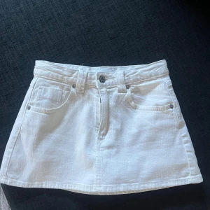 Vit jeanskjol med shorts från Stradivarius - Säljer en vit jeanskjol från Stradivarius med inbyggda shorts under. Kjolen har klassisk femficksdesign, bälteshällor och knapp med dragkedja framtill. Perfekt för dig som vill ha en fräsch och bekväm look. Passar till sneakers eller boots. Aldrig använd och säljer då den va för liten för mig 🥰