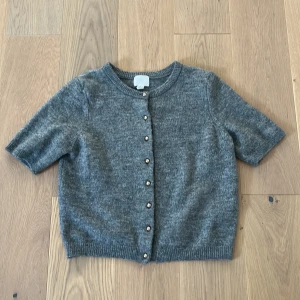 Grå stickad kofta från H&M - Säljer en grå stickad kofta från H&M i storlek S. Koftan har korta ärmar och rund hals, snygga pärlknappar framtill🩷