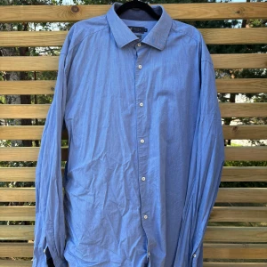 Blå skjorta från Riley slim fit XXL - Snygg blå skjorta från Riley i slim fit-modell, storlek XXL. Skjortan har klassisk krage, vita knappar och är tillverkad i mjuk bomull med lite stretch för extra komfort. Perfekt för dig som gillar stilrena och enkla plagg.