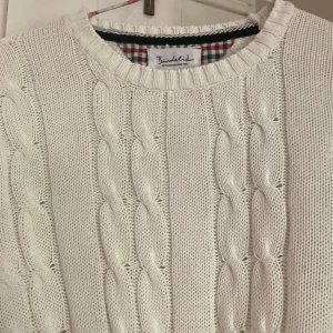 Vit kabelstickad tröja från Bondelid - Säljer en vit kabelstickad tröja från Bondelid i storlek S. Tröjan har rund hals, ribbade muddar och ett snyggt brunt märke vid nederkanten. Perfekt för dig som gillar klassisk stil och vill ha något mjukt och skönt i garderoben.