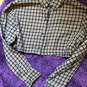 Rutig croppad skjorta från H&M Divided, S - Snygg croppad skjorta från H&M i brunt och svart rutigt mönster. Skjortan har klassisk krage, långa ärmar och knäppning framtill. Sitter även croppad på XS.