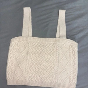 Beige stickad linnetopp från H&M - Superfin beige stickad linnetopp från H&M med breda axelband och snyggt flätmönster framtill. Perfekt att styla med jeans eller kjol för en chill och trendig look. Mjuk och skön känsla tack vare det stickade materialet.