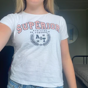 Vit t-shirt Superior 157, bomull - Vit t-shirt från 157 med trycket 'SUPERIOR Athletes of Tomorrow' i rosa och svart på bröstet. Rund hals och korta ärmar, tillverkad i 100% bomull. Snygg sportig vibe med grafiskt tryck och relaxed passform. Perfekt till jeans eller shorts.