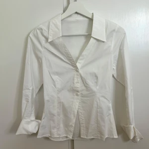 Vit figursydd skjorta - Klassisk vit figursydd skjorta med lång ärm och knappar framtill. Perfekt för en clean och stilren look. Storlek XS och helt oanvänd. 