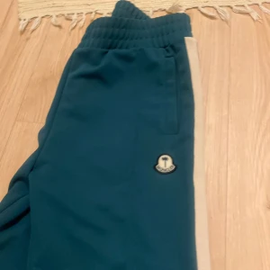  blå mjukisbyxor - Snygga blå mjukisbyxor från  med vita sidoränder och broderad logga framtill. Byxorna har elastisk midja och dragkedja vid benslut. Perfekta för en chill och sportig look.