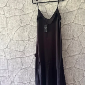 Svart långklänning med smala axelband - Svart långklänning från NA-KD med smala axelband och v-ringad hals. Klänningen har en stilren och minimalistisk design i mjukt, glansigt material som ger en lyxig känsla. Perfekt för dig som gillar enkel elegans och vill sticka ut med en klassisk look. Katt finns i hemmet 