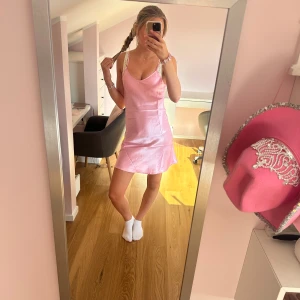 Rosa satin klänning med smala axelband - Supersöt rosa kort klänning i satin med smala justerbara axelband och v-ringning. Klänningen är lite lätt utsvängd så den funkar både som en vanlig klänning och en pyjamas!!💕💕