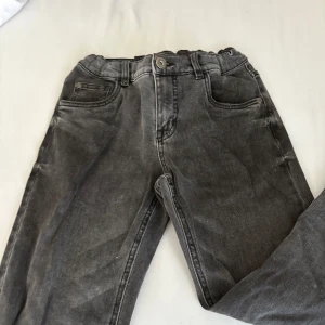 Grå jeans från LAB Industries, stl 152 - Snygga grå jeans från LAB Industries i storlek 152. Modellen har klassisk femficksdesign, elastisk midja och raka ben. Jeansen har en cool tvättad look och passar perfekt till en avslappnad streetstyle. Materialet är slitstarkt jeans och färgen är mörkgrå.