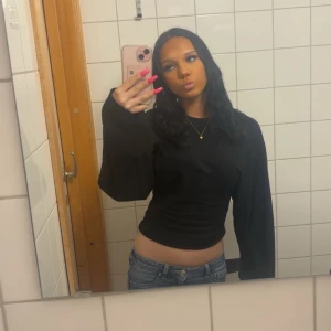 Svart croppad långärmad tröja - Svart  tröja med långa, vida ärmar och lite tajtare i midjan. Snygg och enkel design som passar till jeans eller kjol. Materialet känns mjukt och stretchigt, perfekt för dig som gillar en stilren look med lite edge.