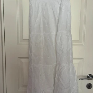 Vit långkjol med broderade detaljer - Supersöt vit långkjol från Gina Tricot med broderade blommor och smock i midjan. Kjolen har en luftig och flowy känsla, perfekt för varma dagar. Materialet är mjukt och har fina spetsdetaljer som ger en romantisk vibe.