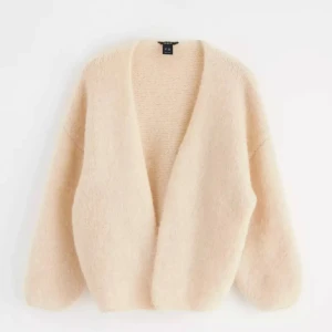 Beige fluffig kofta från Lindex  - Supermjuk och oversized beige kofta från Lindex. Koftan har en öppen front utan knappar, lång ärm och är stickad i ett fluffigt material som känns lyxigt och mysigt. Perfekt att slänga på sig när det är kyligt ute. Lite noppig