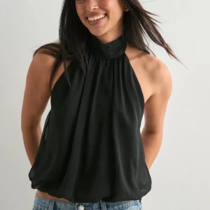 Svart halterneck linnetopp - Säljer en svart halterneck linnetopp med hög krage och lös passform. Toppen är ärmlös och har en snygg, luftig känsla som passar perfekt till jeans eller kjol. Materialet känns lätt och flowy, vilket ger en cool vibe.