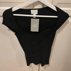 Svart ribbad topp från H&M - Svart snygg ribbad topp från H&M med urringning och korta ärmar. Gjord i stretchigt material. Perfekt att styla med nästa allt. Har lånat bilderna från tjejen jag köpte den av. Säljer den för att den tyvärr inte passade när jag fick hem den. Skriv gärna vid frågor!