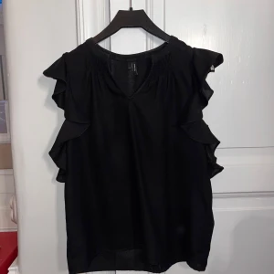 Svart blus med volang från Vero Moda - Snygg svart blus med volanger från Vero Moda. Säljer för att den inte kommer till mycket användning och använd ett fåtal gånger!