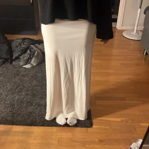 Vit långkjol från Gina Tricot  - Säljer en stilren vit långkjol från Gina Tricot i storlek XS. Kjolen har en rak och flowy passform med slät yta och är gjord i ett mjukt syntetmaterial. Perfekt för dig som gillar minimalistisk och clean stil.