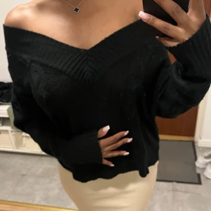 Svart offshoulder stickad tröja - Säljer en svart stickad tröja med offshoulder-design och bred ribbad kant vid halsen. Tröjan har lång ärm och en loose passform som ger en chill och snygg vibe. 