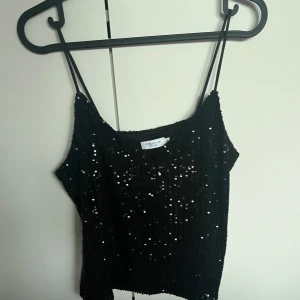 Svart paljettopp från Stockh LM Studio - Säljer en svart glittrig linne-topp från Stockh LM Studio i storlek XS. Topp med tunna axelband och täckt av paljetter som ger en riktigt festlig känsla. Perfekt för dig som vill sticka ut och glänsa lite extra.