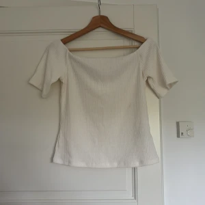 Offshoulder ribbad topp i vitt - Superfin offshoulder topp i vitt med ribbad struktur och korta ärmar. Storlek L men passar M och S då den är liten i storleken. Sitter snyggt över axlarna och har en enkel, stilren look som passar perfekt till jeans eller kjol. Mjuk och skön, perfekt för varmare dagar.