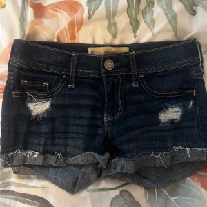jeansshorts från Hollister - Snygga mörkblå jeansshorts från Hollister med slitna detaljer och fransig kant. Klassisk femficksmodell med gul kontrastsöm och uppvikta ben. Perfekta för chill dagar och sommarhäng. Passar dig som gillar en avslappnad och trendig stil. Pris går att diskutera om❤️