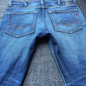 Replay Jondrill jeans blå, stl 28  - Säljer ett par snygga Replay Jondrill jeans i klassisk blå tvätt. Jeansen har raka ben, fem fickor och coola kontrastsömmar på bakfickorna. Märkespatch i rött på insidan och Replay-logga vid fickan. Perfekta för dig som gillar stilrena jeans med modern passform.