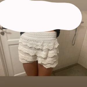 Vita virkade shorts med volang - Superfina trendiga  vita shorts med virkade detaljer och flera lager volanger. lågmidjade och med bred resår i midjan för skön passform. Perfekta till sommaren när du vill ha en söt och luftig look. Materialet är bomull! Det är från spanien så vet inte exakta märket, köpta för 600kr pris kan diskuteras!💓🥰