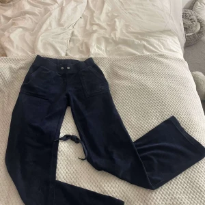 Mörkblå Juicy Couture mjukisbyxor - Mörkblå mjukisbyxor från Juicy Couture med broderad logga på fickan. Byxorna har bred resår i midjan med snörning, stora fickor fram och bak med knappdetaljer. Mjukt och skönt material som passar perfekt för chill dagar. De är i storlek xxs men jag som med storlek M kan ha dom dom passar även för personer med storlek S.