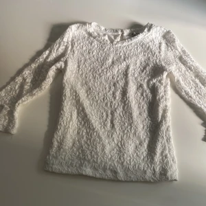 Vit spetsblus med blommigt mönster - Superfin vit blus med lång ärm och blommigt spetsmönster över hela plagget. Blusen har rund halsringning och är fodrad i kroppen men transparent i ärmarna. Perfekt för dig som gillar romantisk och stilren look.