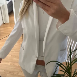 Vit kavaj från Gina Tricot, strl 36 - Snygg vit kavaj från Gina Tricot i klassisk modell med en knapp framtill och två fickor. Stilren och enkel design med mjukt tyg som känns skönt mot huden. Perfekt att styla med jeans eller kjol för en fräsch look.