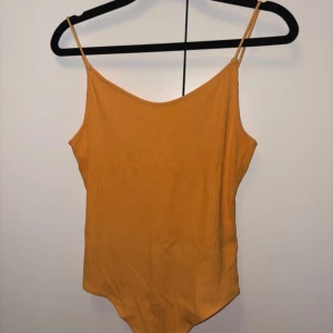 Orange ribbad linnetopp från H&M - Snygg orange ribbad linnetopp från H&M med smala axelband och djup rygg. Perfekt för varma dagar och enkel att matcha med jeans eller kjol. Toppens material är mjukt och stretchigt för en bekväm passform.